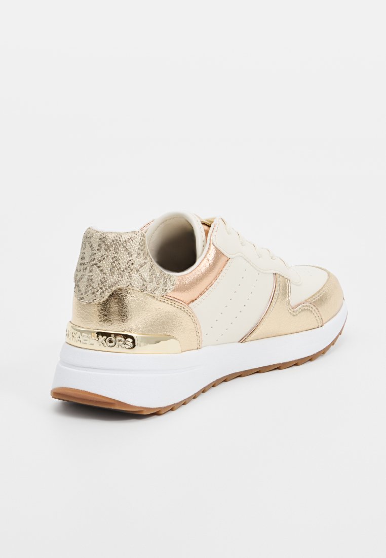 Baskets avec tige en cuir crème, accents métalliques dorés, arrière texturé et semelle blanche. Comprend un détail de logo doré sur le talon.