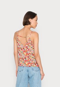 Top sem mangas floral com design em V nas costas. Apresenta um padrão colorido sobre um fundo claro. Feito de um tecido suave e leve.