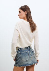 Kermansävyinen neulepaita pyöreällä pääntiellä, yhdistetty vaaleansiniseen farkku minihameeseen, jossa on takataskut ja rispaantunut helma.