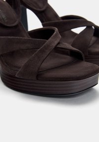 Brown suede high-heeled sandals with crisscross straps, platform sole, and ribbed texture detail on the base.