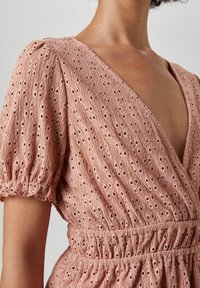 Rosenfarbenes, strukturiertes Kleid mit kurz puffärmeligen Ärmeln, einem tiefen V-Ausschnitt und durchgehenden Lochmuster-Details. Verstellbarer Bund für eine figurschmeichelnde Passform.
