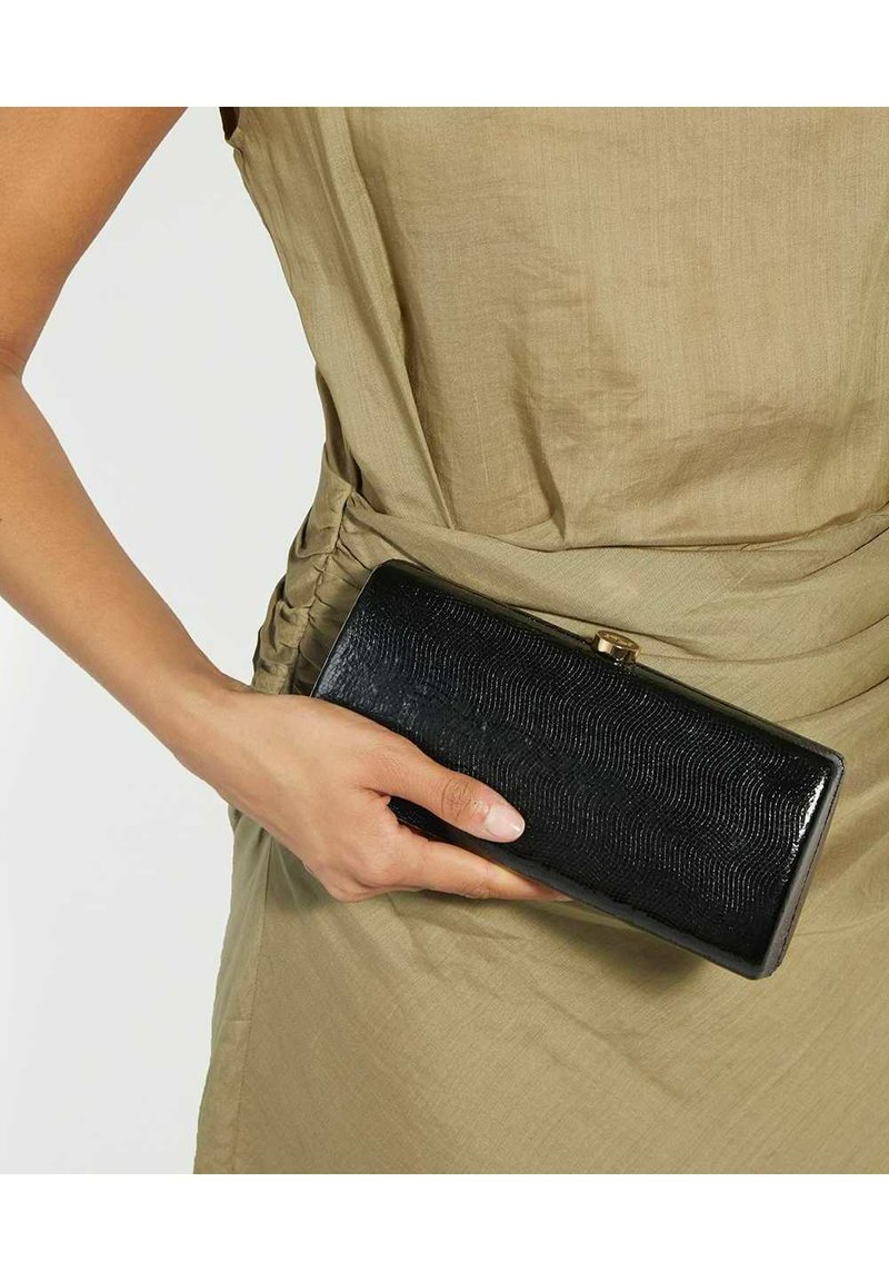 Black textured wallet with a wavy pattern, rectangular shape, glossy finish, and gold clasp detail, held in a hand against a beige fabric backdrop.