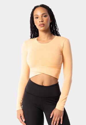 Meruňkový crop top s dlouhým rukávem a stočeným předním designem, kombinovaný s černými legínami s vysokým pasem. Hladká bavlněná směs tkaniny.