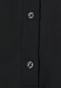 Tissu de chemise noire à boutonnière avec une texture lisse, doté d'une patte à deux boutons et de boutons plats à quatre trous.