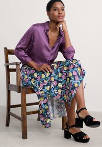 Purple satin blouse with a collar, paired with a flowy blue skirt featuring a floral pattern in yellow, pink, and green. Black block-heeled sandals.