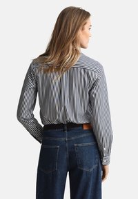 Gestreept overhemd met knopen in marineblauw en wit, gecombineerd met donkerblauwe jeans. Heeft een rechte pasvorm en lange mouwen, met een achterkantdetail met ingezette rugpas.