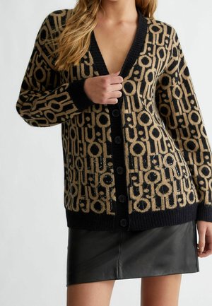 Woman wearing a black and beige patterned buttoned cardigan with a deep V-neck and a black leather mini skirt.