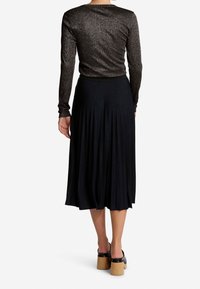 Långärmad, mörk metallisk topp med rund halsringning, parat med en svart plisserad midikjol och kraftiga svarta klacksandaler.