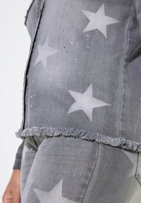 Jeansjacka med grå stjärnmönster, prydd med rhinestones, har fransade kanter och en figursydd design för en modern look.