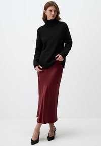 Maglione a collo alto in maglia nera abbinato a una gonna midi in satin bordeaux e tacchi alti neri, caratterizzato da un design rilassato e dettagli a costine.