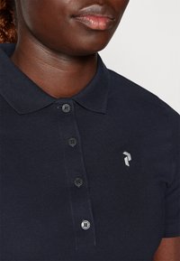 Polo azul-marinho com colarinho canelado, quatro botões e um pequeno logótipo bordado no lado esquerdo. O tecido parece texturizado e respirável.
