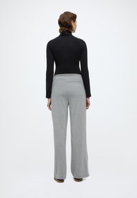 Μαύρο μακρυμάνικο τοπ ζιβάγκο σε συνδυασμό με ανοιχτό γκρι, άνετο παντελόνι με ελαστική μέση, με απλό φόντο.