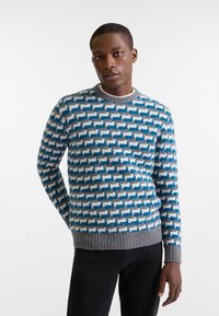 Maglione lavorato a maglia con un motivo geometrico blu, grigio e bianco. Orlo e polsini grigi a coste, scollatura rotonda. Realizzato in tessuto morbido e dalla consistenza particolare.