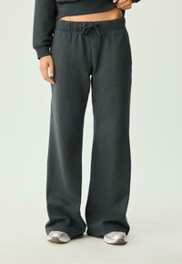 Donkergrijze, wijde sweatpants met een elastische tailleband en trekkoord. Zacht stof met een gladde textuur. Gepaard met zilveren sneakers.