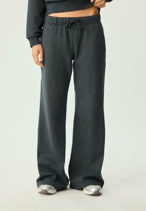 Dunkelgraue, weit geschnittene Sweatpants mit elastischem Bund und Kordelzug. Weicher Stoff mit glatter Textur. Kombiniert mit silbernen Sneakers.