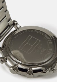 Le fond de montre en acier inoxydable présente un logo gravé, un numéro de modèle et des détails sur la résistance à l'eau. Surface lisse et brillante avec des accents métalliques.