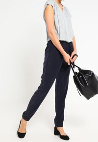 Námořnické modré zúžené kalhoty s elastickým pasem, zkombinované se světle šedou blůzkou s krátkými rukávy a jemným vzorem. Černé vysoké podpatky a kabelka.