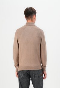 Pull en col roulé beige avec un design côtelé sur les épaules, texture douce et manches ajustées ; porté avec un jean foncé légèrement déchiré.