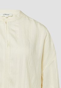 Blouse couleur crème avec des rayures verticales subtiles, encolure ronde, patte de boutonnage partielle, et manches longues de la marque s.Oliver.