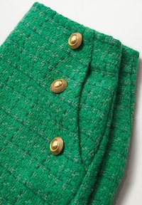 Tissu texturé vert avec un motif en chevrons, comportant trois boutons décoratifs en ton doré à l'avant.