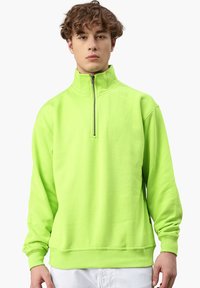 Limegrüner Pullover mit hohem Kragen, Viertelreißverschluss und gerippten Bündchen. Hergestellt aus weichem Stoff mit lässiger Passform.