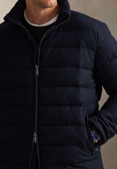 Tamsiai mėlyna su pūkeliu siūta striukė su aukštu apykakliu ir sidabriniu užtrauktuku. Yra šoninės kišenės ir logotipas krūtinės srityje. Tekstūruota medžiaga.