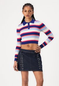 Pull côtelé court avec des rayures bleues, rouges et crème ; associé à une jupe en denim noir avec des côtés à lacets et des œillets en argent.
