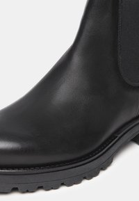 Sort læder ankelstøvle med en glat overflade, elastisk sides Trim og en robust gummisål, der har en subtil glans og rund tå.