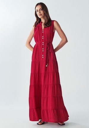 Rotes Maxikleid mit Knopfleiste, gestuftem Design, gebundenem Taillengürtel, ärmellosem Stil und strukturiertem Muster. Sandalen sind am unteren Rand sichtbar.