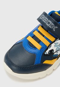Blaue und gelbe Turnschuhe mit einem Wolf-Design, aus synthetischem Material mit strukturierter Oberfläche, Klettverschluss und geformter weißer Sohle.