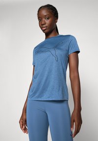 Blå sportt-shirt med en svart PUMA-logotypdesign på framsidan. Kort ärm, tillverkad av mjukt tyg, i kombination med blå tights.