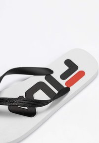Sort flip-flop sandal med en tekstureret hvid sål, der har et stort sort logo og en rød accent. Letvægtsdesign med gummistropper.