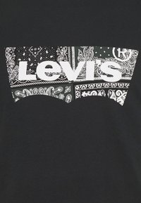 Levi's logotyp i fet vit text över en svart bakgrund fylld med vita paisleymönster och bandanamönster.