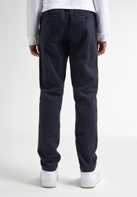 Marineblauwe katoenen broek met een slim fit, voorzien van twee achterzakken met knopen en een gladde textuur. Gestyled met witte sneakers.