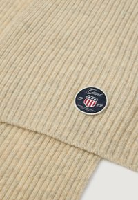 Sudadera de punto beige con canalé, con un parche redondo azul marino que presenta un emblema blanco y rojo, mostrando el nombre de la marca "Grant" y el año "1949".
