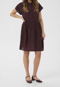 Robe fleurie bordeaux à manches courtes, taille froncée et boutonnée sur le devant. Associée à des chaussures slingback brillantes couleur bordeaux foncé. Texture lisse.