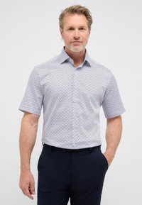 Korte mouwen shirt in lichtblauw met een geometrisch patroon, met een button-down kraag en een ontspannen fit, gecombineerd met donkere broeken.