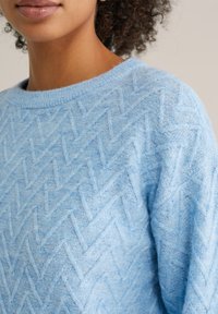 Jasnoniebieski sweter z dzianiny z teksturowanym wzorem zygzakowym, szerokim dekoltem i opadającymi ramionami, wykonany z miękkiego, przytulnego materiału.