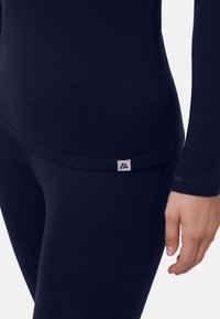 Marineblaues Langarmoberteil aus glattem Stoff, mit figurbetontem Schnitt und kleinem Markenlabel an der Naht.