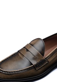 Mocassin en cuir marron avec une finition lisse, comportant une bande cousue et un motif découpé sur le fermoir. Semelle en caoutchouc noir.