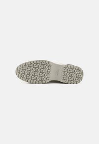 Sneaker beige chiaro con una suola in gomma grigia texture, caratterizzata da un motivo di battistrada triangolare e un design minimalista.
