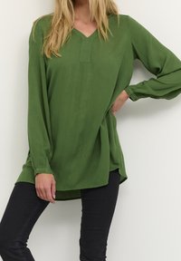 Groene blouse met lange mouwen en een V-hals, gemaakt van lichtgewicht stof, met een losse pasvorm en zijslits, gecombineerd met zwarte broek.