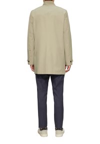 Beige, middellang jasje met een rechte snit, twee zijzakken, knoopaccenten op de mouwen, gedragen over marineblauwe broek en sneakers.