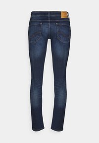 Jeans de mezclilla azul oscuro con corte ajustado, con bolsillos traseros y una etiqueta de marca de cuero en la cinturilla. Textura suave con un leve desgastado.