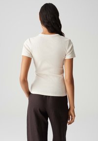 Top aderente a maniche corte in tessuto a coste color crema, con scollatura rotonda e orlo dritto, abbinato a pantaloni scuri larghi.