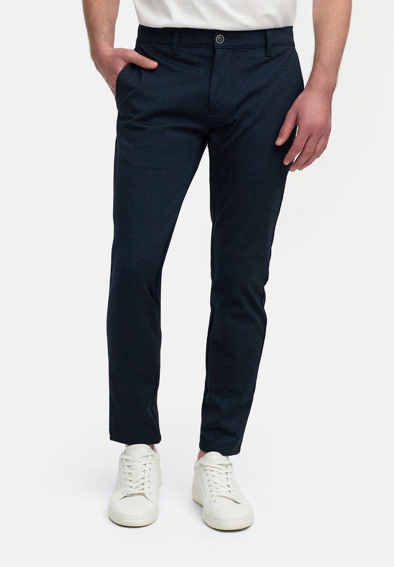 Marineblauwe slim-fit broeken van textuurstof, met zijzakken, knoopsluiting en gestyled met witte sneakers.