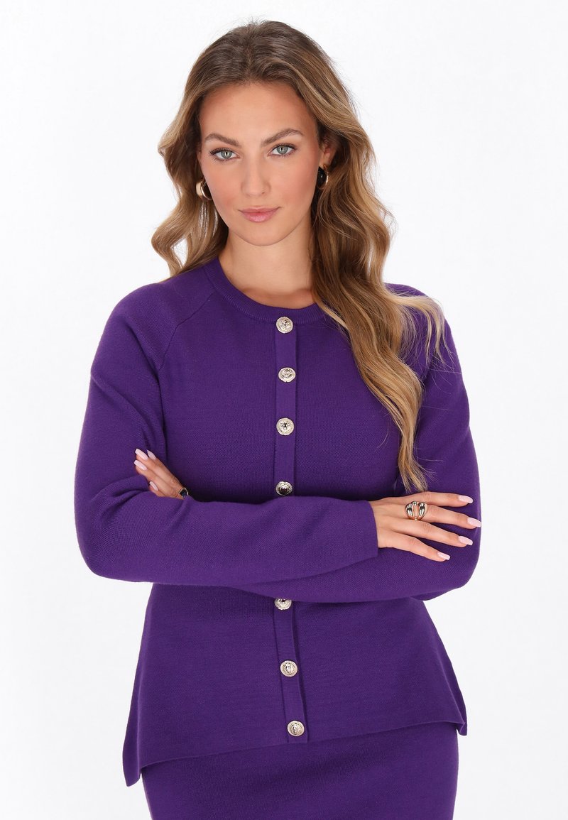 Cardigan lavorato a maglia viola con scollo rotondo, caratterizzato da bottoni argentati sulla parte anteriore e un orlo posteriore leggermente più lungo.