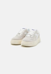 Sneaker grigie chiare con texture in camoscio, dettagli bianchi e perforazioni. Presentano un classico sistema di allacciatura e una suola spessa di colore crema.