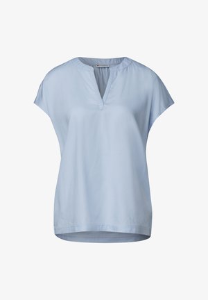 Ljusblå kortärmad blus med V-ringning, tillverkad av en mjuk tyg. Har mjukt rullade kanter nära axlarna och en rundad nederkant.
