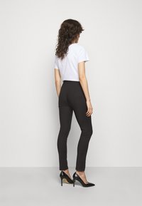 Pantaloni neri attillati con vita alta, abbinati a una t-shirt bianca corta. L'outfit presenta una texture liscia e un design semplice.